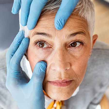 An older female patient receiving a physical eye exam from a doctor wearing gloves